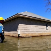 House foundation with water nearby, builder overseeing construction.